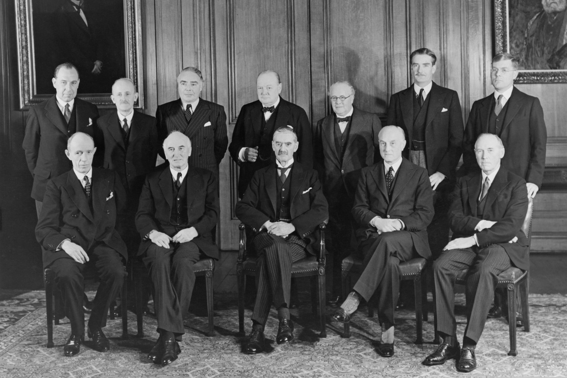 Прем’єр Невіл Чемберлен (сидить у центрі) серед урядовців свого кабінету. Тоді ще перший лорд Адміралтейства Черчилль стоїть за Чемберленом, листопад 1939 року.
