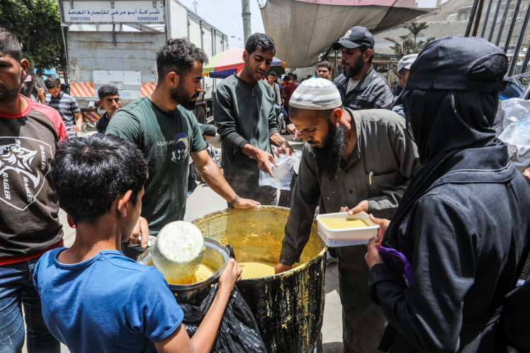 Палестинці у місті Дейр-аль-Балах у Газі стоять у черзі, щоб отримати їжу, яку роздають благодійні організації, 18 травня 2024 року.