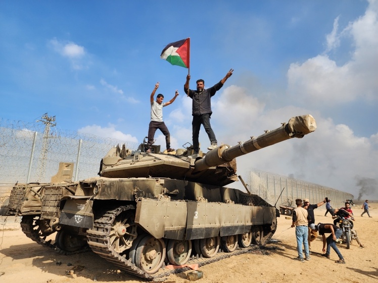Hamas soldiers hold a Palestinian flag on an Israeli army tank. Gaza City, October 7, 2023.