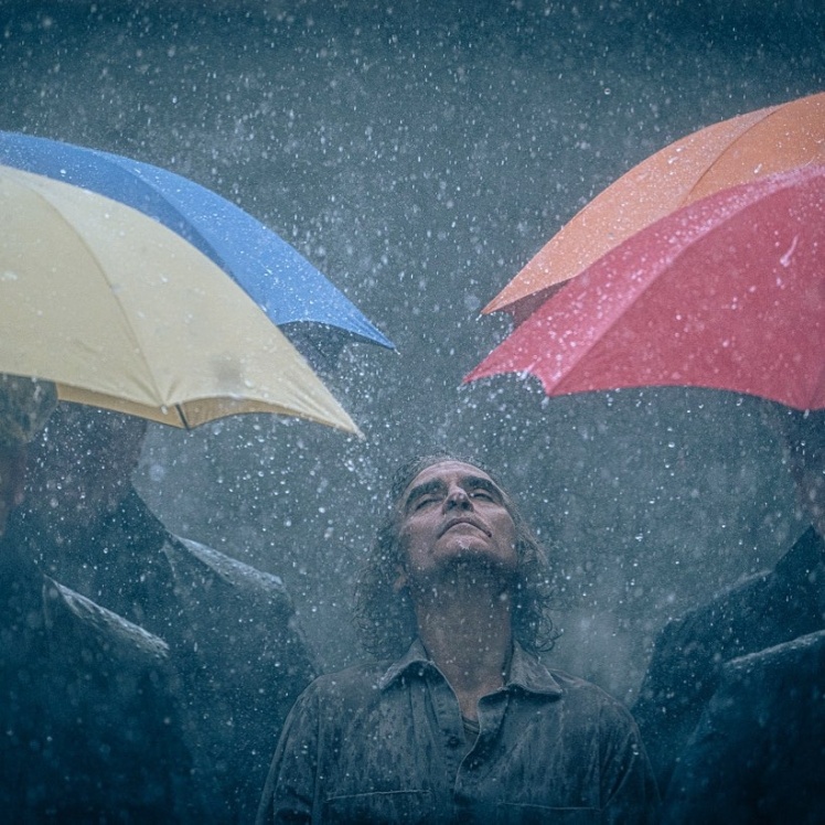 Самотній головний герой мокне під дощем в оточенні людей з кольоровими парасольками.