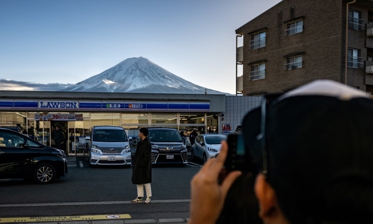 A tourist poses in front of a Lawson store with Mount Fuji in the background. It is here that they want to install a protective barrier.