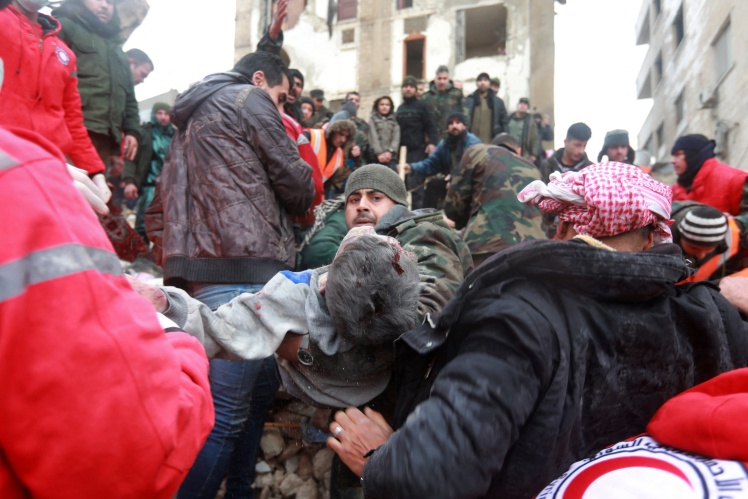 Сирійські рятувальники несуть постраждалого, якого вдалося витягти з-під завалів у місті Хама.