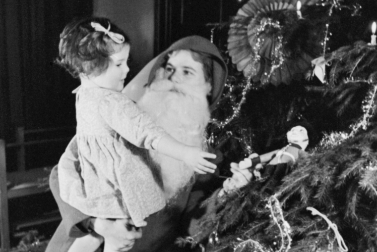 An American woman in a Santa costume greets a child with Merry Christmas, 1941.