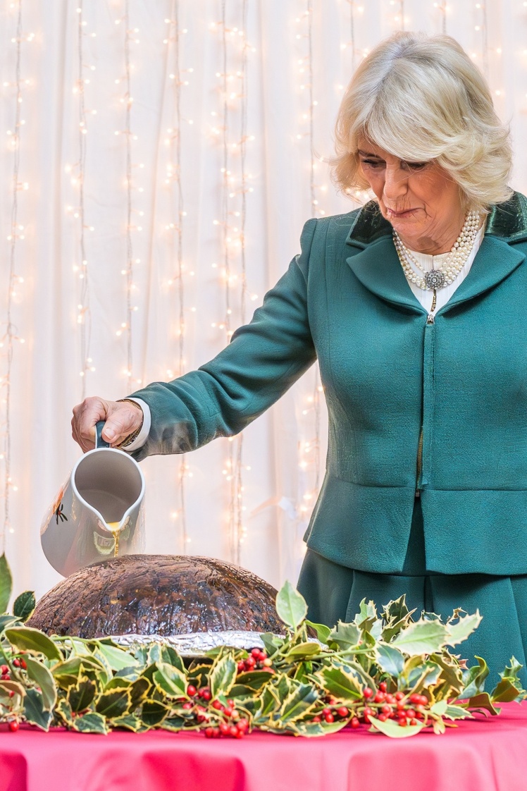 Королева Камілла поливає святковий пудинг соусом.