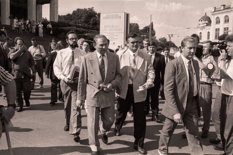 Леонід Кучма виходить з Українського дому з першої пресконференції після виборів. За ним, ліворуч у білій сорочці — керівник штабу Дмитро Табачник. Праворуч у чорному піджаку — Олександр Волков. Київ, 13 липня 1994 року.