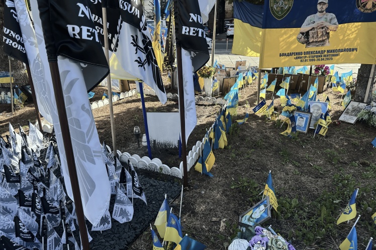 Someone has enclosed the area with a white garden fence, where there is a photo of the deceased, lamps, and cookies.