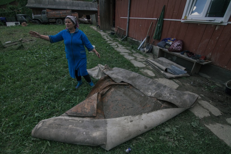 Вода залила сараи для скота и подвалы домов, а в некоторых домах поднялась по щиколотку. Местная жительница показывает грязный линолеум, который она вытащила из дома после потопа.