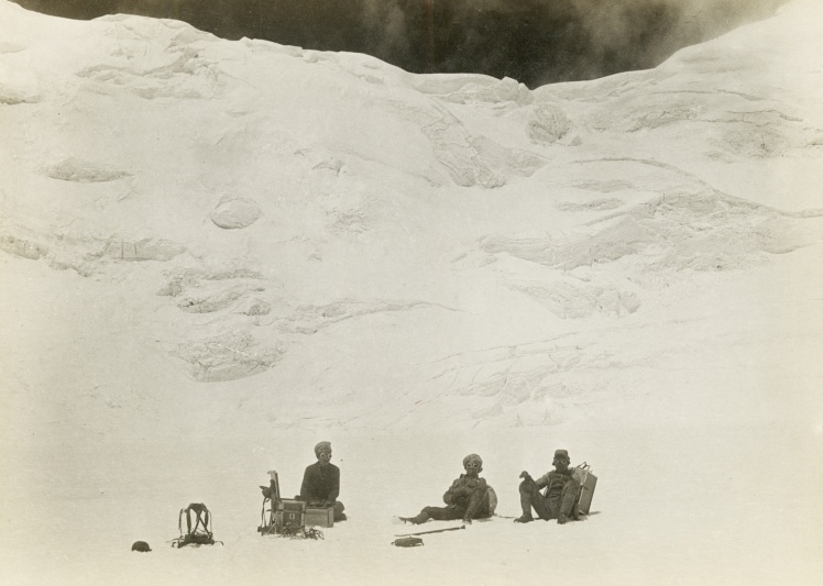 Группа шерпов отдыхает на снегу во время британской экспедиции на Эверест 1924 года.