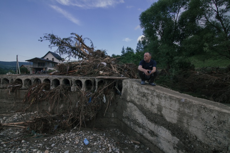 Житель Черного Потока Василий сидит вблизи разрушенного моста.