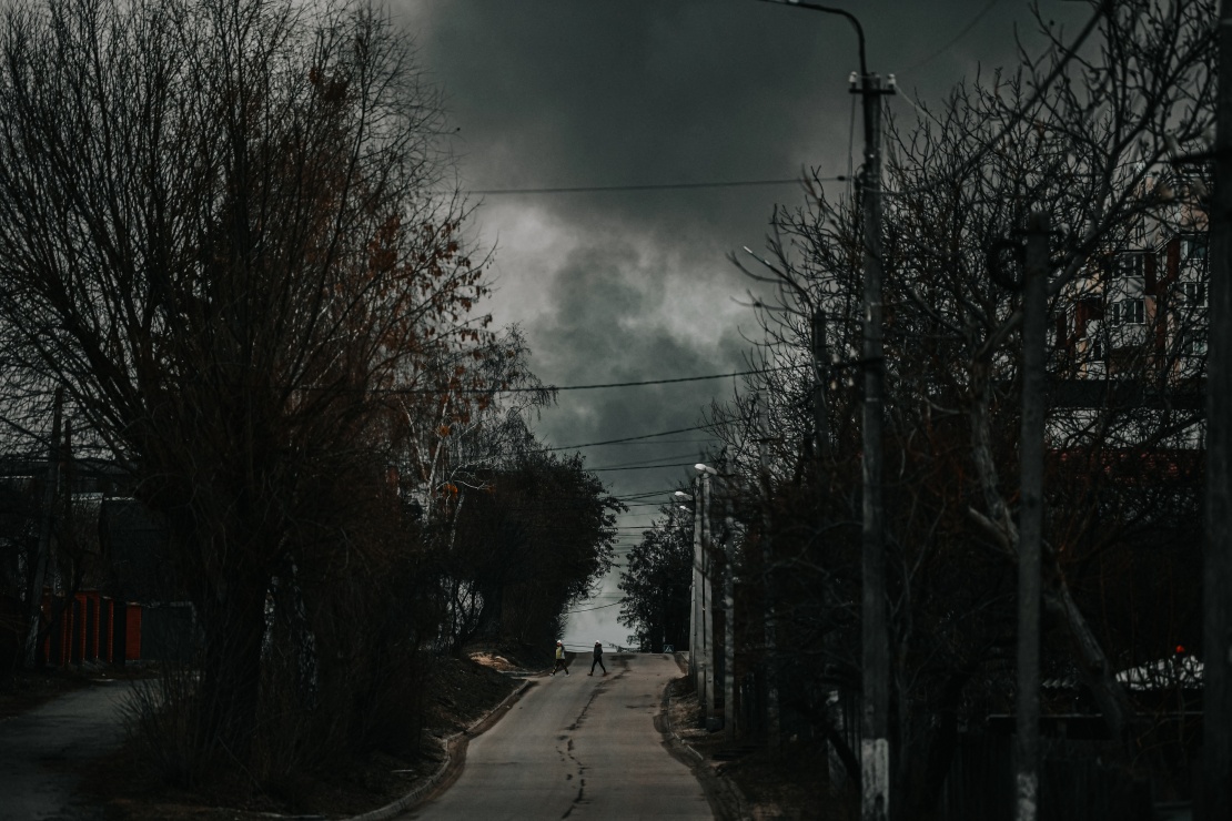 Місцеві мешканці переходять дорогу у Гостомелі в той час, як над аеропортом Антонова піднімається дим