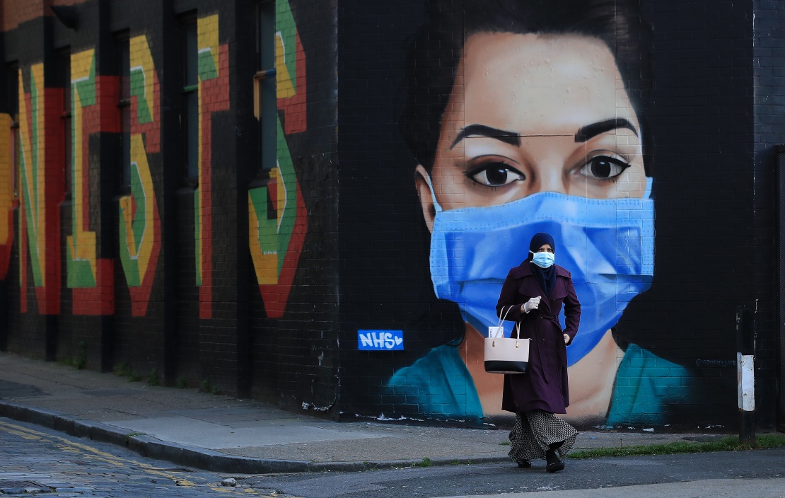 Женщина в защитной маске проходит мимо граффити,&nbsp;изображающего врача Национальной службы здравоохранения Великобритании, Лондон, 21 апреля 2020 года.
