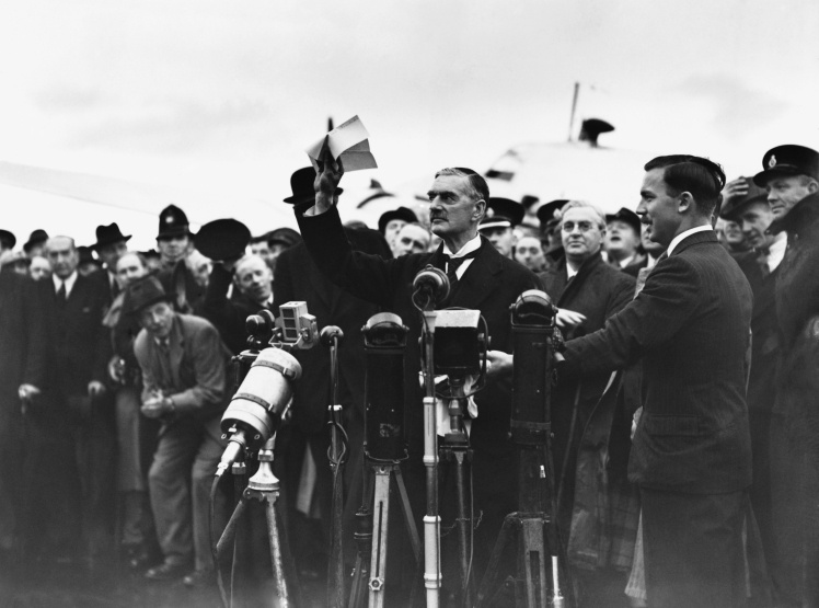Премьер-министр Невилл Чемберлен машет рукой толпе в аэропорту «Хестон» и декламирует речь «Мир для нашего поколения» после возвращения с подписания Мюнхенского соглашения, 30 сентября 1938 года.