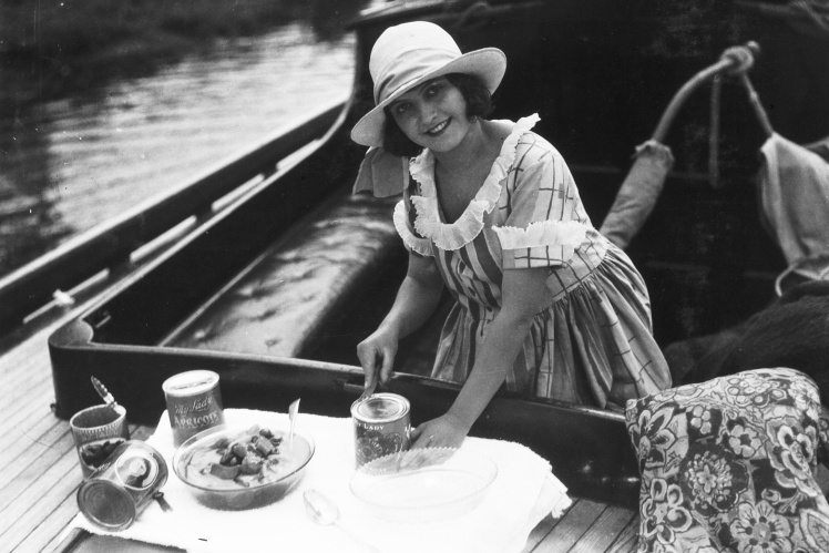 Жінка відкриває консервним ножем бляшанки з консервованими абрикосами, 1920-ті роки.