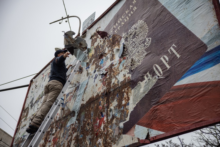 Чоловік зриває плакат із російською пропагандою в Херсоні.