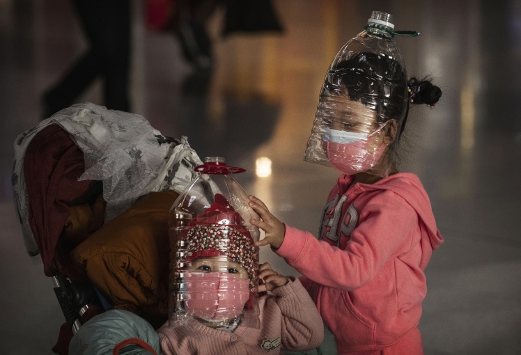 Китайские дети в самодельных защитных масках из пластиковых бутылок стоят в очереди в пекинском аэропорту, 30 января 2020 года.