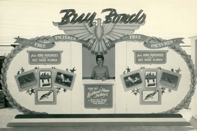 A woman stands behind a counter advertising war bonds, 1942.