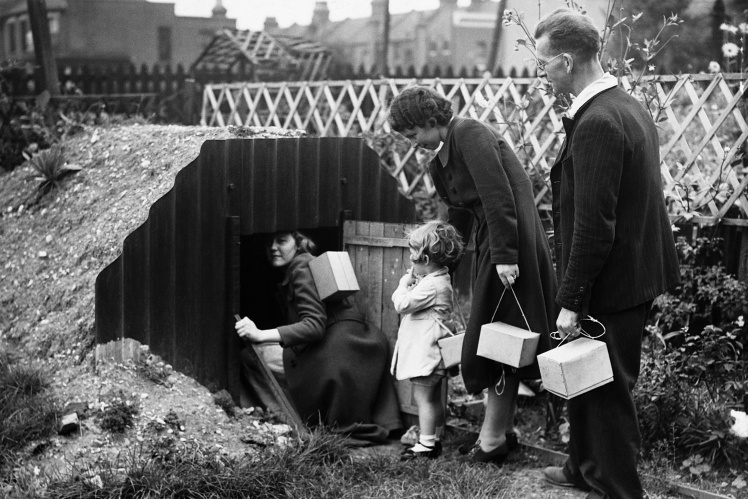A British family with gas masks in boxes goes down to a bomb shelter in their own garden, 1939.