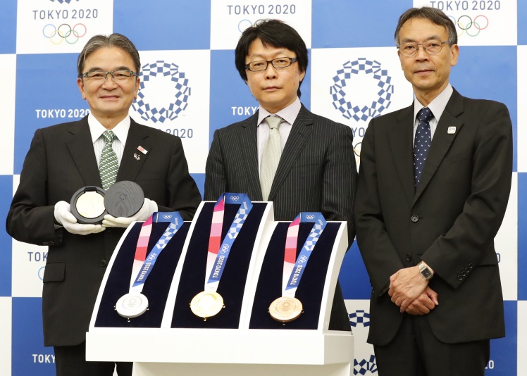 Автор дизайну медалей для Олімпійських ігор у Токіо 2020 року Юнічі Каванісі (у центрі) з комплектом олімпійських нагород, 25 липня 2019 року.